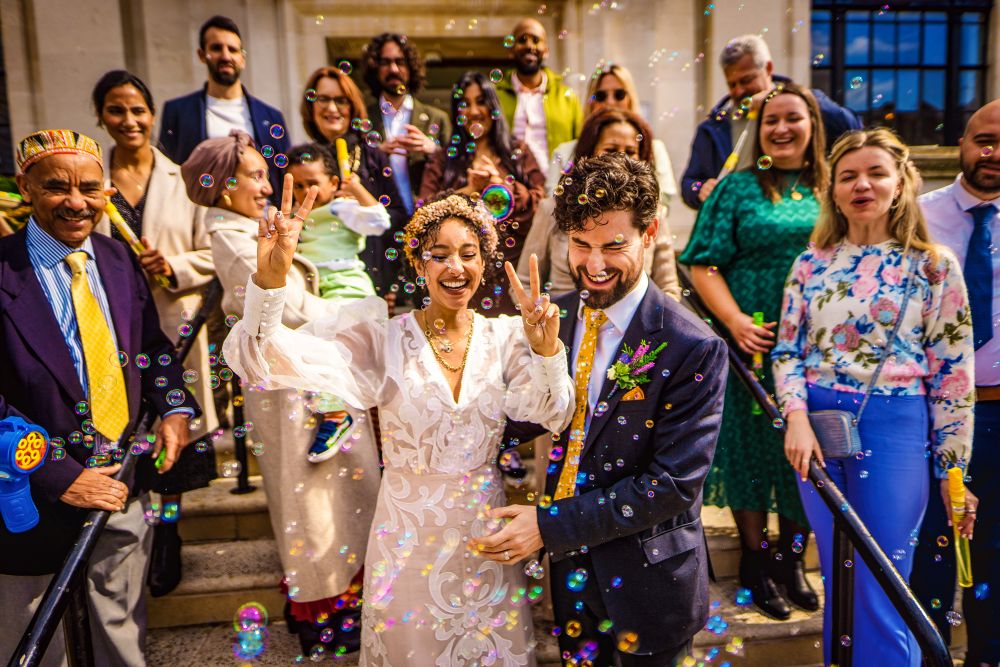 A newly married couple celebrating with guests and bubbles on the steps of Islington Town Hall